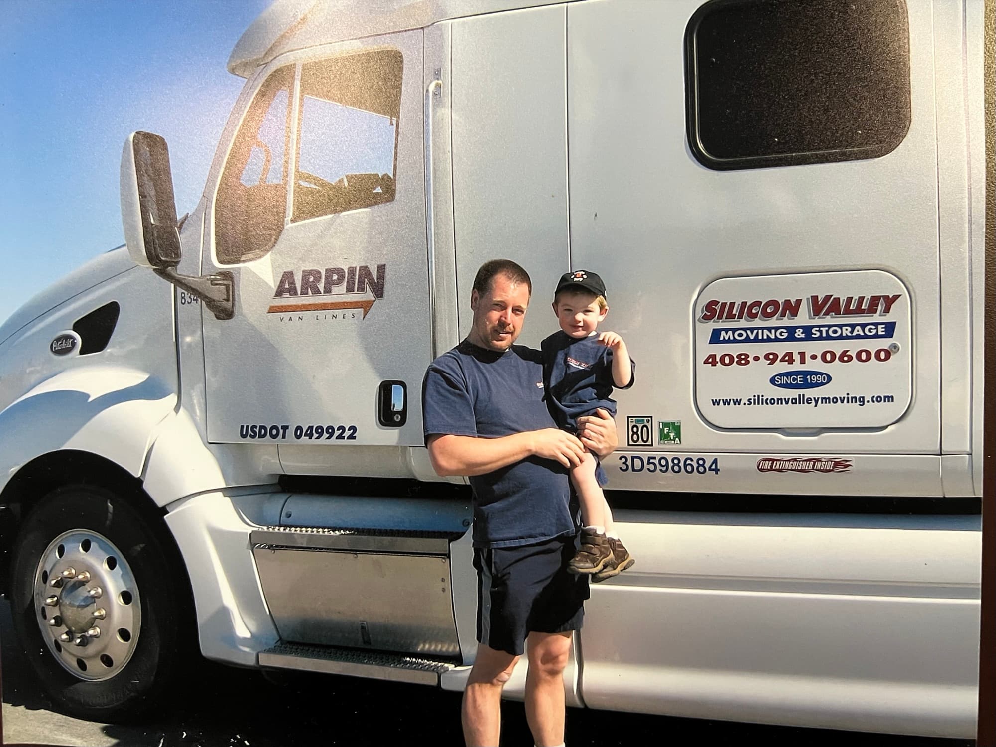 Silicon Valley Moving & Storage owner Joe Childs holding his young son Joey in front of a company truck showing the Since 1990 decal