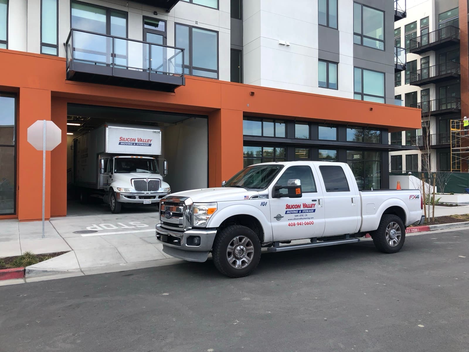 Silicon Valley Moving & Storage box truck reversed into a modern San Jose apartment complex loading dock with a co-branded SVM pickup parked in the foreground