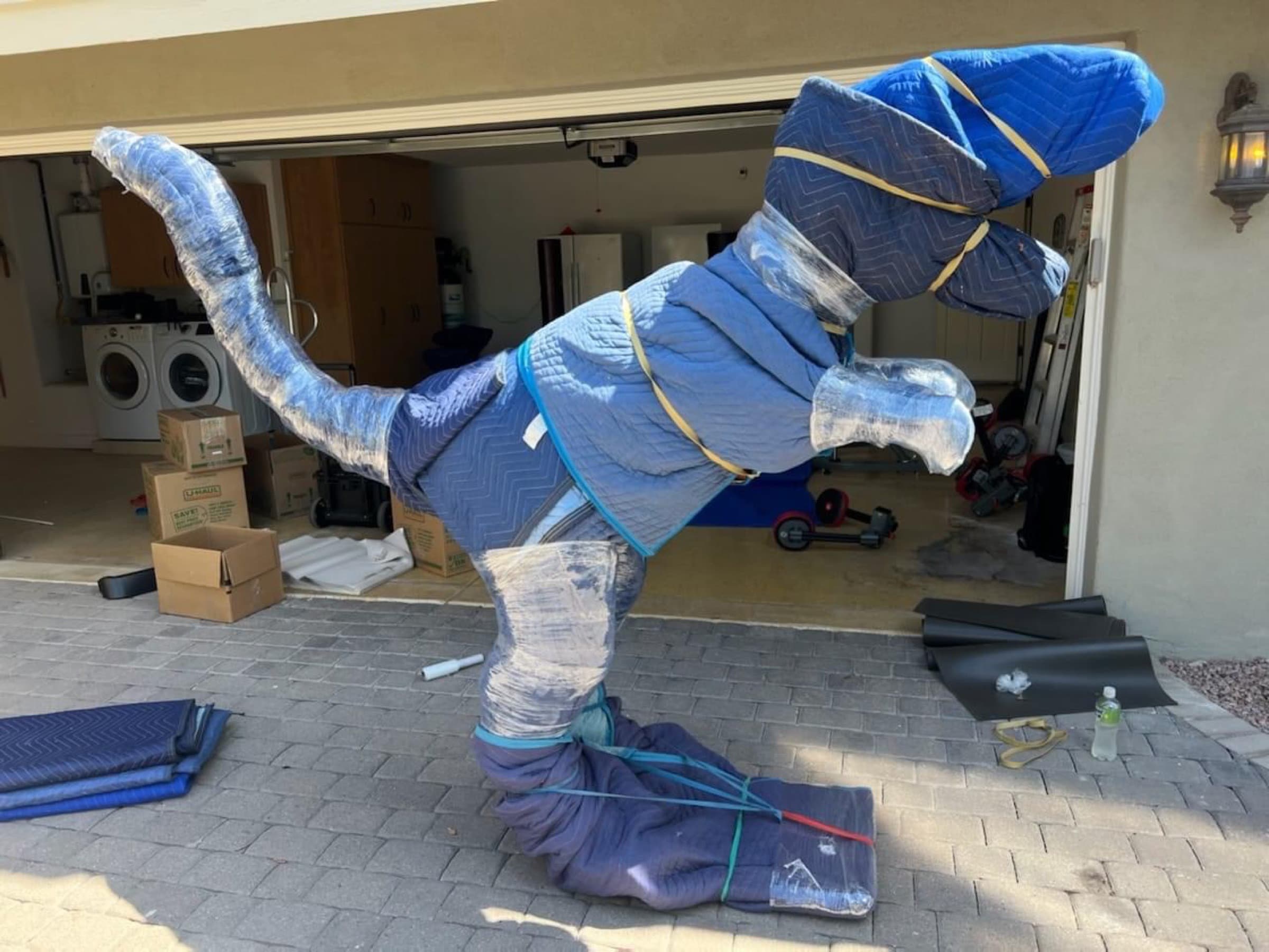 A ten-foot-tall dinosaur sculpture fully wrapped in furniture pads, stretch wrap, and banding in a driveway, prepped for a specialty move by Silicon Valley Moving & Storage